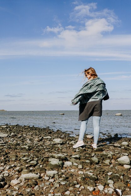 Mujer joven con gafas de sol envuelto en una bufanda de otoño en el golfo de Finlandia