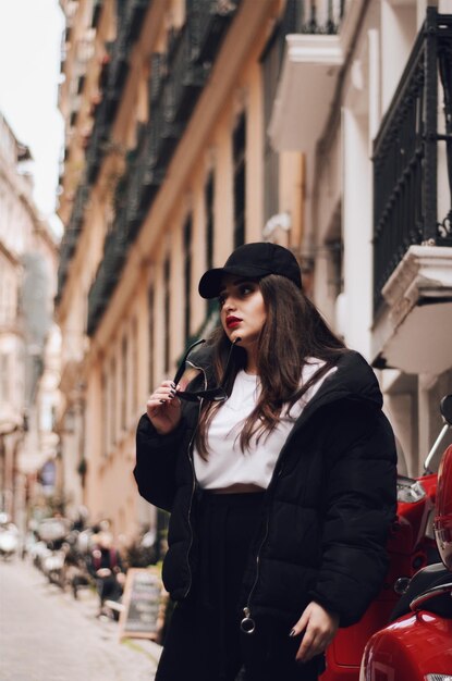 Mujer joven con gafas de sol mientras está de pie contra un edificio en la ciudad