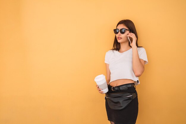 Foto mujer joven con gafas de sol de pie contra la pared