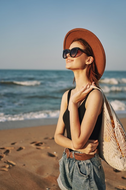 Mujer joven con gafas de sol de pie en la playa contra el cielo