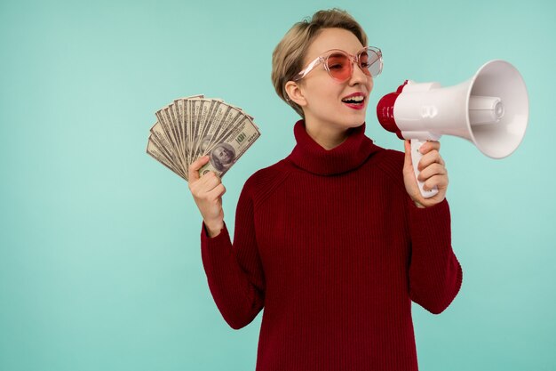 Mujer joven en gafas de sol rosa con dinero gritando al altavoz