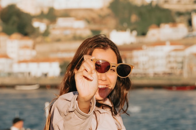 Mujer joven con gafas de sol sonriendo mucho mientras las toca, concepto de gafas de sol, verano y viajes, espacio de copia