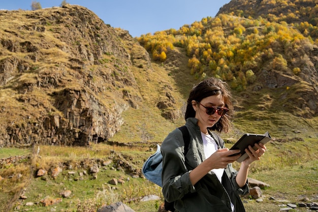 Mujer joven con gafas de sol usando una tableta para elegir el camino mientras camina por las montañas
