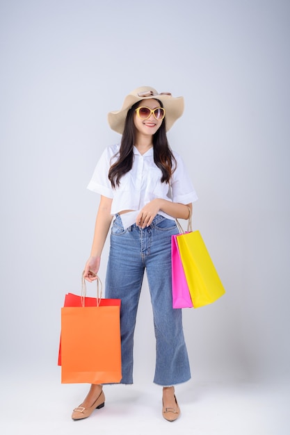 mujer joven con gafas y un sombrero lleva una bolsa de compras y una factura mientras mira hacia el lado aislado sobre fondo blanco.