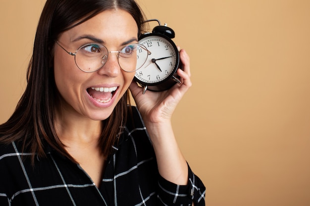 Foto una mujer joven con gafas sosteniendo un reloj despertador.