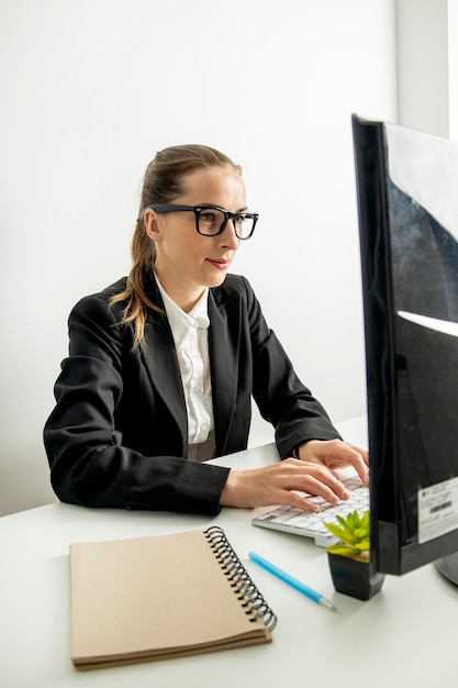 Mujer joven con gafas trabajando sentada en la computadora en el lugar de trabajo