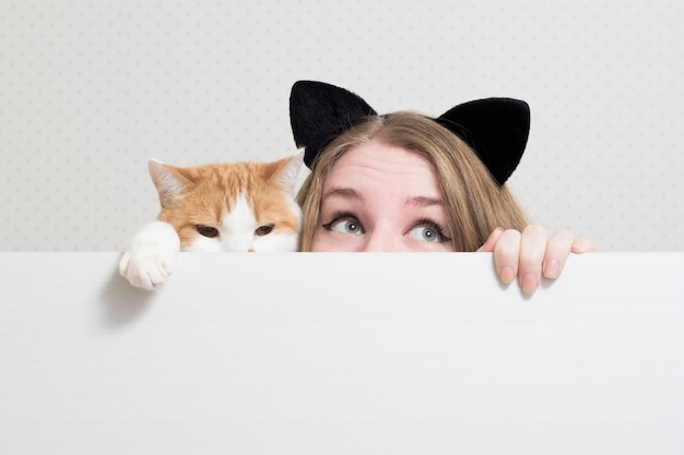 Foto mujer joven con gato se esconden detrás de una pancarta blanca