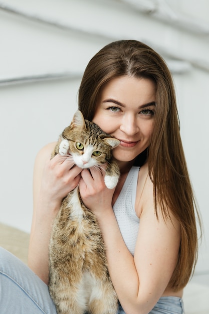 Mujer joven con gato sentado en la cama. Chica en dormitorio de luz.