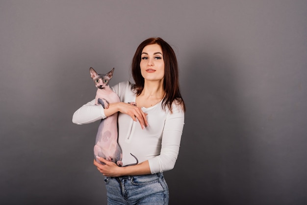 Mujer joven con gato sphynx canadiense en un estudio, fondo gris