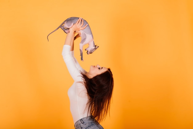 Mujer joven con gato sphynx canadiense en un estudio, fondo gris