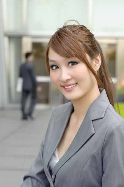 Mujer joven gerente de negocios de Asia sonriendo y mirándote, retrato de detalle de media longitud fuera de los edificios modernos.