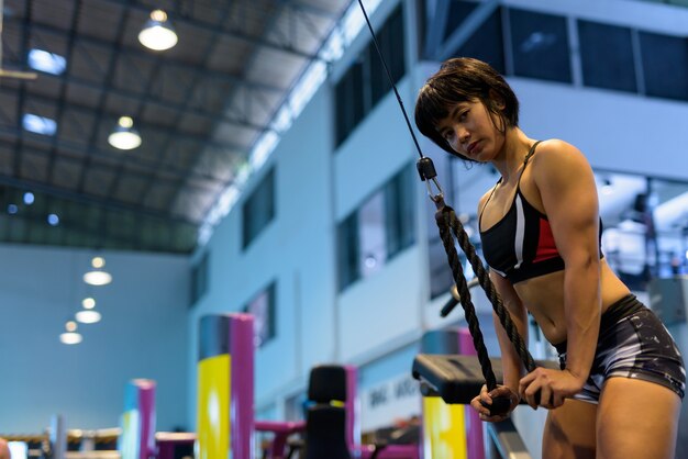 Mujer joven en el gimnasio haciendo pushdown de tríceps con cuerda