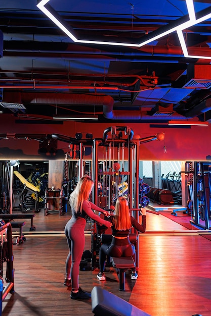 Mujer joven en el gimnasio realiza ejercicios bajo la guía de un entrenador experimentado. Una forma de vida sana.