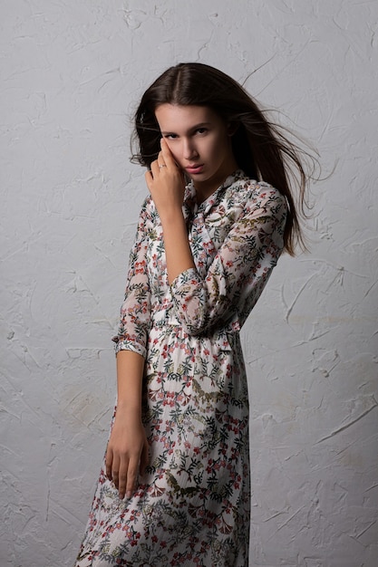 Mujer joven glamorosa viste vestido de moda posando con el pelo ondeando en la pared gris