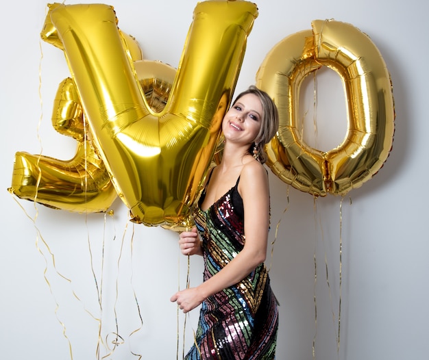 Mujer joven con globos dorados en su cumpleaños de treinta años. La persona está en vestido y peinado vintage 80.