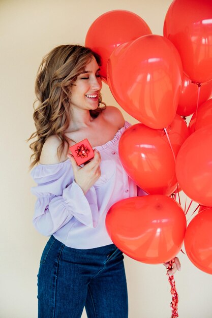 Una mujer joven con globos en forma de corazón y una caja de regalo El concepto de las vacaciones del 8 de marzo y el Día de San Valentín