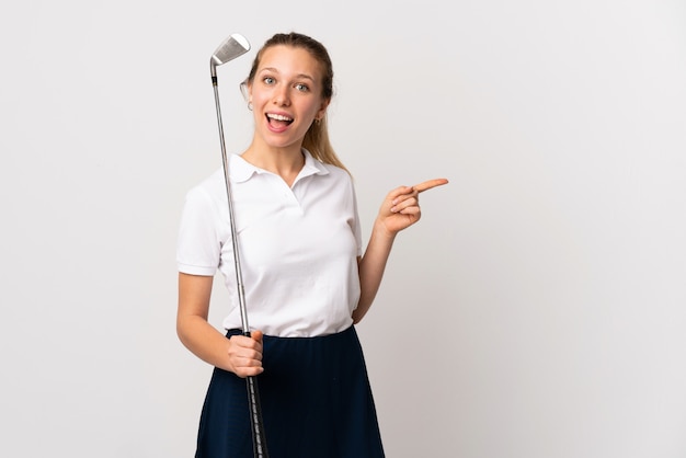 Mujer joven golfista sobre la pared blanca aislada que señala el dedo al lado