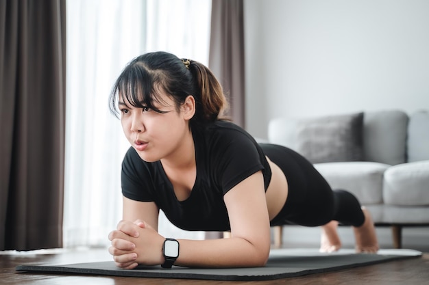 Foto mujer joven gordita asiática haciendo ejercicio de tablones en el interior de su casa xa