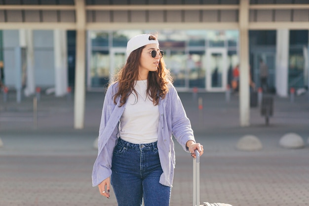 Mujer joven con una gorra blanca con una maleta