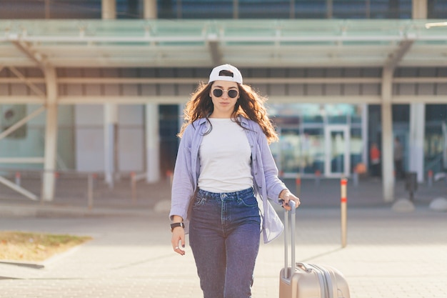 Mujer joven con una gorra blanca con una maleta