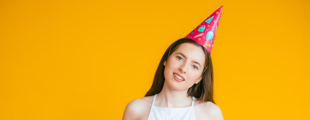 Mujer joven en una gorra de celebración jugando en una fiesta en el fondo amarillo