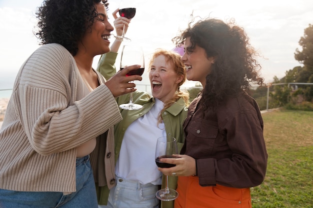 Mujer joven con gorro de fiesta riendo y brindando con sus amigas durante la fiesta al aire libre