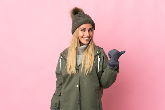 Mujer joven con gorro de invierno en rosa apuntando hacia el lado para presentar un producto