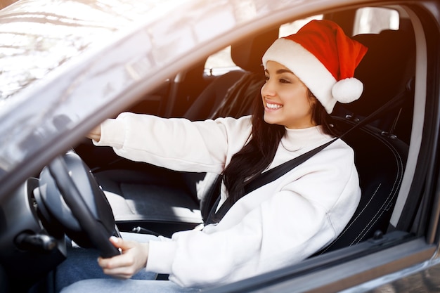 Mujer joven con gorro de Papá Noel conduciendo su coche