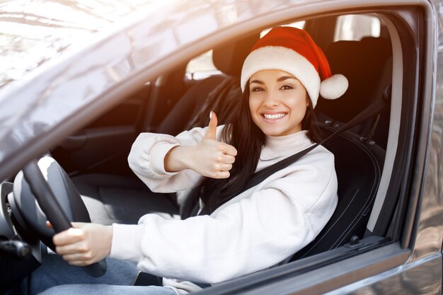 Mujer joven con gorro de Papá Noel conduciendo su coche