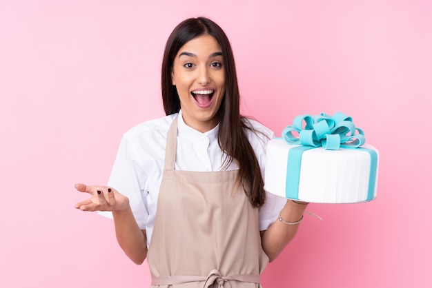 Mujer joven con un gran pastel con expresión facial sorprendida