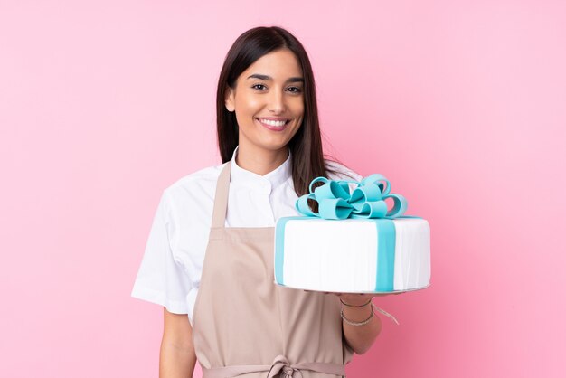 Mujer joven con un gran pastel sobre pared aislada sonriendo mucho