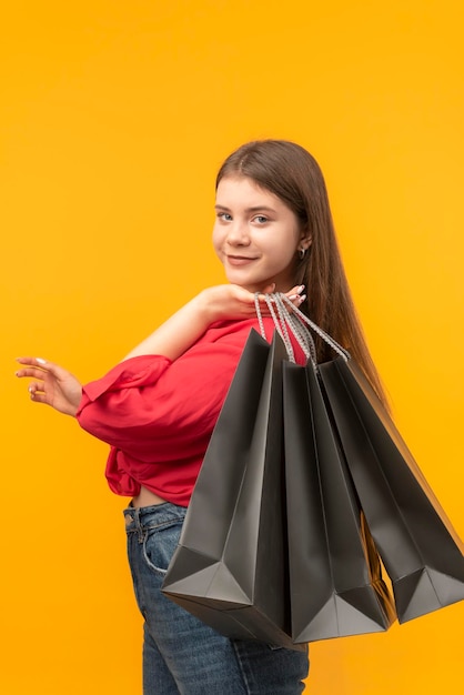 Mujer joven con grandes bolsas de compras negras Mujer sonríe después de buenas compras Fondo amarillo brillante Marco vertical