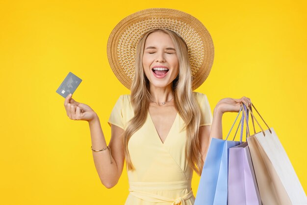 Mujer joven gritando emocionada sosteniendo bolsas de compras y tarjeta de crédito de pie aislado