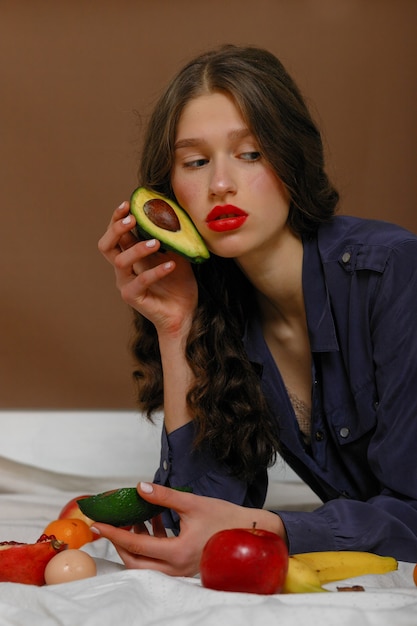 Mujer joven en grupo de frutas. Concepto de salud y nutrición saludable. sostiene un aguacate cerca de la cara
