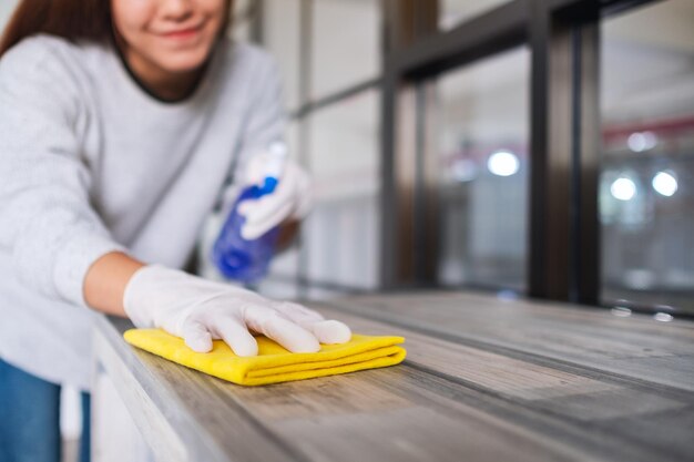 Foto una mujer joven con guante de protección limpiando la mesa para la persona del concepto de trabajo doméstico