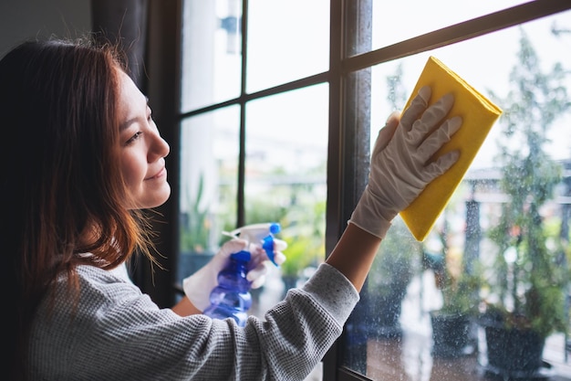 Una mujer joven con guante protector limpiando la ventana para el concepto de quehaceres domésticos