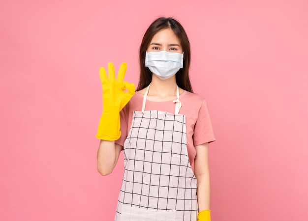 Mujer joven con guantes de goma y muestra el signo de ok sobre fondo rosa