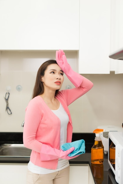 Mujer joven en guantes de goma rosa limpiando una superficie de armario de cocina blanco