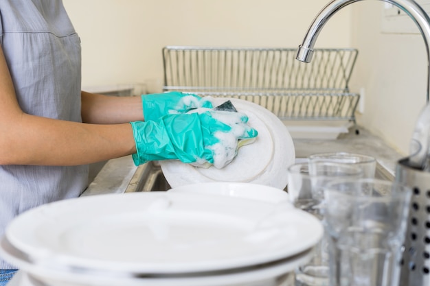 Mujer joven con guantes lavando platos