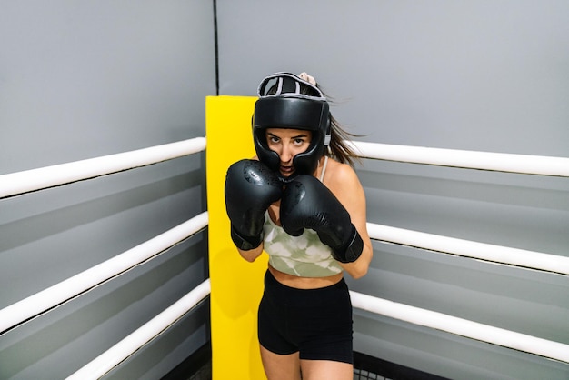 Una mujer joven con guantes protectores de boxeo y casco en posición de combate en un cuadrilátero de boxeo