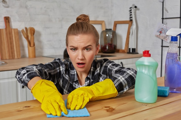 Mujer joven con guantes protectores limpia una mesa en la cocina con un trapo