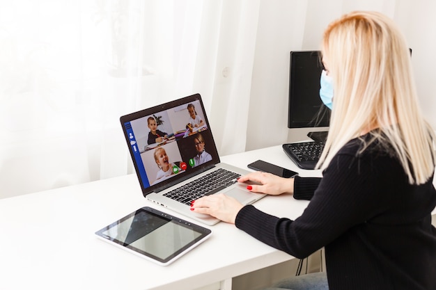 Mujer joven con guantes protectores en las manos y máscara en la cara trabajando desde casa o en el trabajo de oficina por la videollamada de la computadora portátil para prevenir la propagación de virus, prevención de cuarentena epidémica