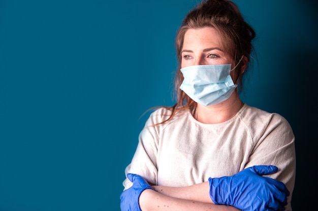 Mujer joven con guantes protectores y mascarilla dentro de una casa en cuarentena con aspecto aburrido y triste, por Covid-19 Coronavirus