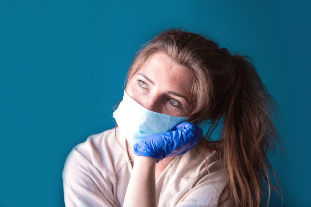 Mujer joven con guantes protectores y mascarilla dentro de una casa en cuarentena con aspecto aburrido y triste, por Covid-19 Coronavirus