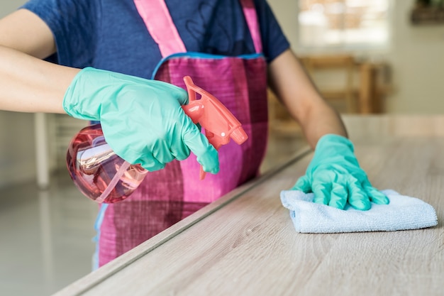 Mujer joven en guantes protectores usando un plumero y aerosol