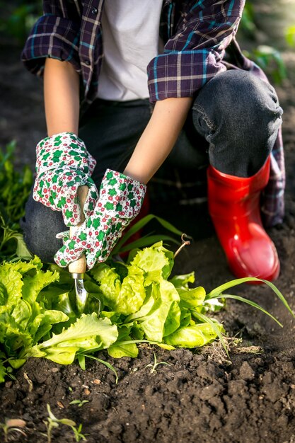 Mujer joven en guantes trabajando en jardín con pala de metal