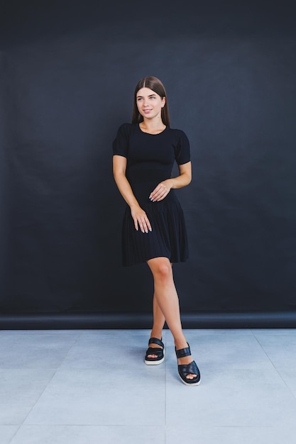 Una mujer joven y guapa con un vestido corto negro y sandalias de cuero ligero Moda de verano para mujeres