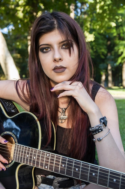 Mujer joven con una guitarra acústica en el parque