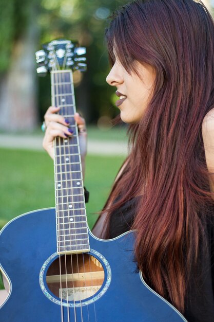 Mujer joven con una guitarra acústica en el parque