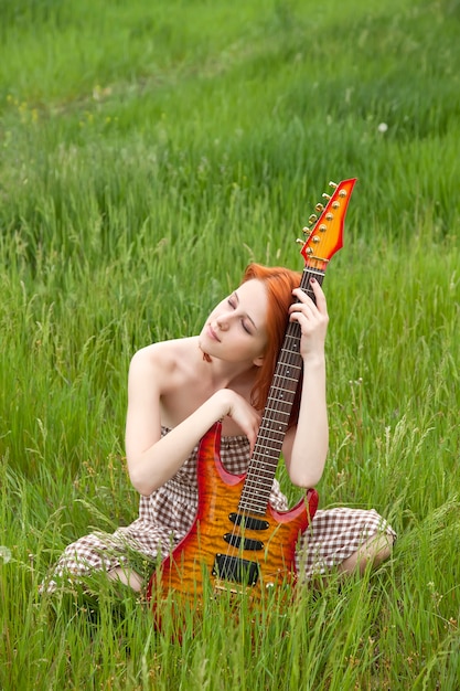 Mujer joven con guitarra en campo de trigo verde